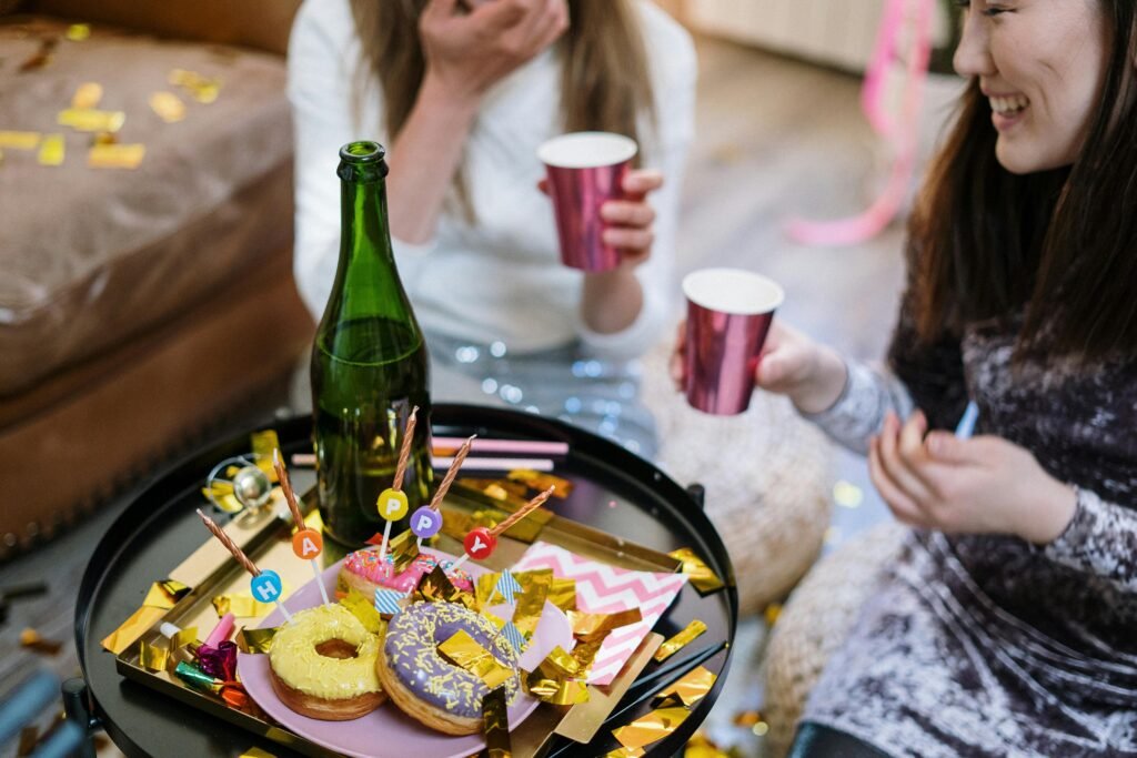 Women celebrating a birthday with doughnuts and drinks indoors, creating a joyful and festive atmosphere.